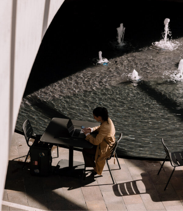 A woman sits at a table working by a fountain.