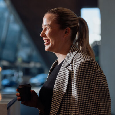 A woman smiles whilst holding a cup of coffee.
