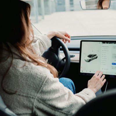 A woman driving inside a Tesla car, using the touch screen.