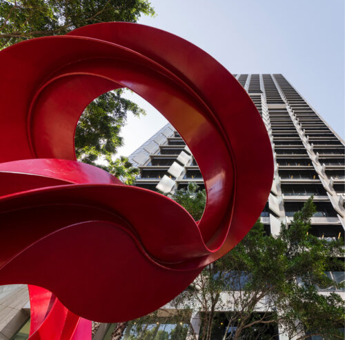 An image of the QV1 building with a red art feature in front of the building.