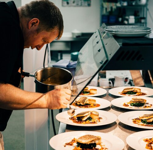 A chef prepares multiple dishes in a kitchen.