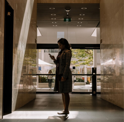 A woman waits for an elevator whilst typing on her phone.